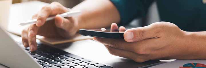 Two hands using a laptop and smartphone